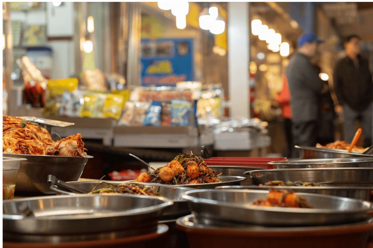 Traditional Korean food stalls at Gwangjang Market featuring kimchi, vegetables, and lively market atmosphere.